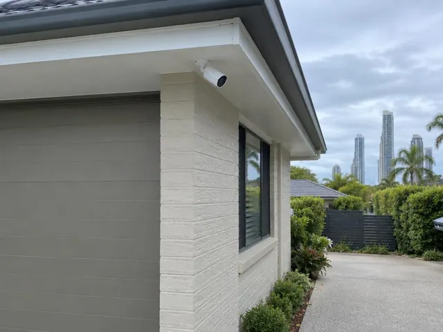 White CCTV camera mounted under an eave on a brick home exterior in Broadbeach