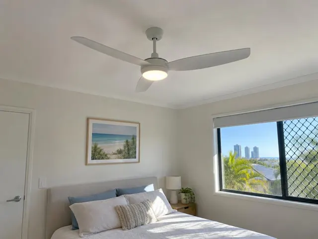 Ceiling fan in a bright bedroom with a bed, window and coastal wall art in Broadbeach