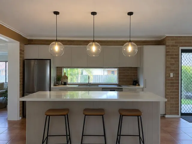 Three glass pendant lights above a kitchen island in a brick-walled home interior in Mermaid Beach