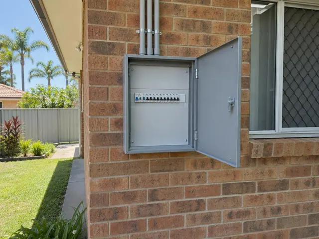 Open external switchboard on a brick house wall beside a window in Mermaid Waters